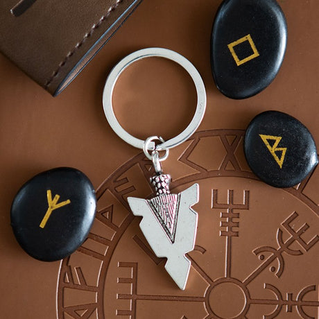 Keychain with arrow design on a brown surface with stones featuring rune symbols