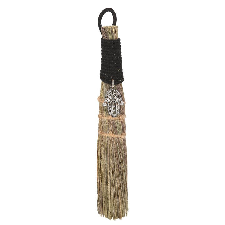 A small traditional broom with a jute string binding and a metal charm, commonly used for spiritual purposes.