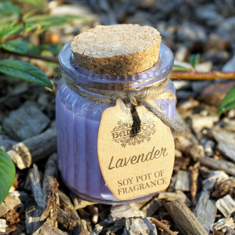 A purple soy candle inside a glass jar with a cork lid, adorned with a brown label that reads 'Lavender SOY POT OF FRAGRANCE'.