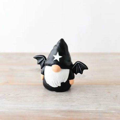 Gonk figurine with black hat, white beard, and bat wings on a wooden surface.