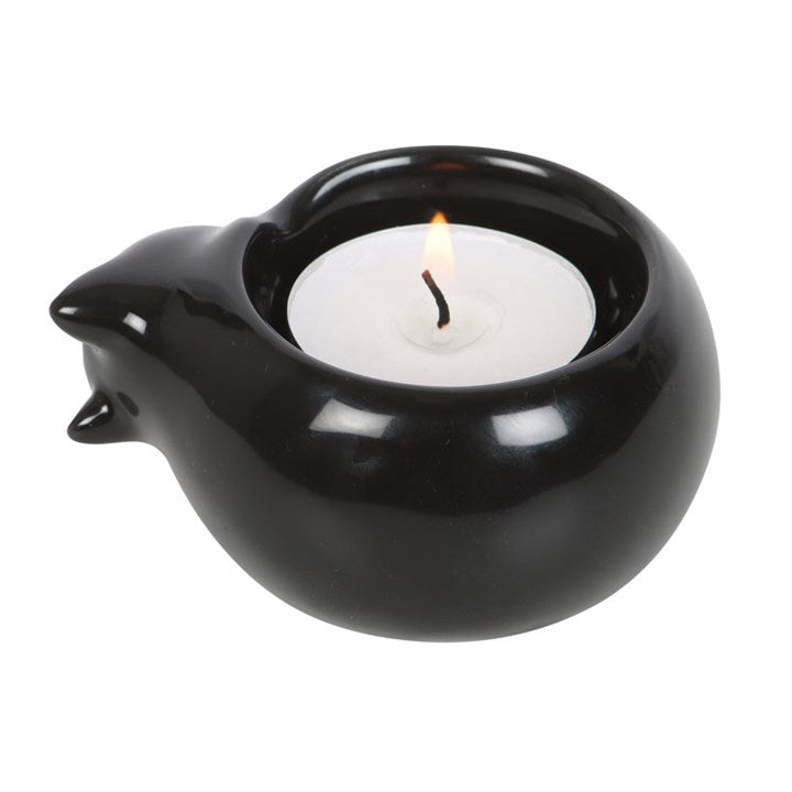 A black cat-shaped tea light candle holder with a lit candle inside, placed on a white surface. 