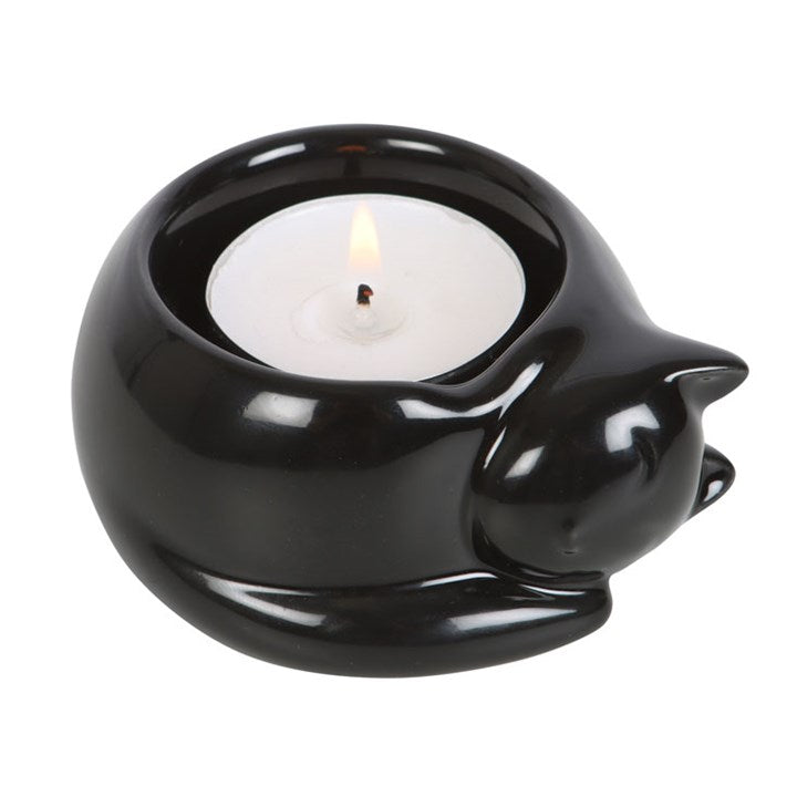 A black cat-shaped tea light candle holder with a lit candle inside, placed on white surface.