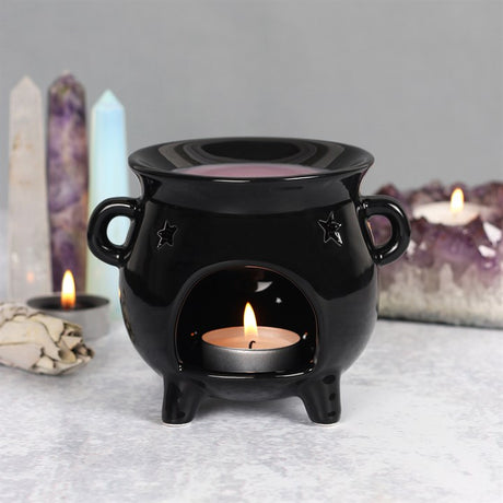 A black cauldron shaped wax burner with a lit tea light inside. There are crystals in the background