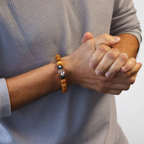 A person's hands clasped together wearing a cedarwood bracelet with a clear quartz bead on the wrist.