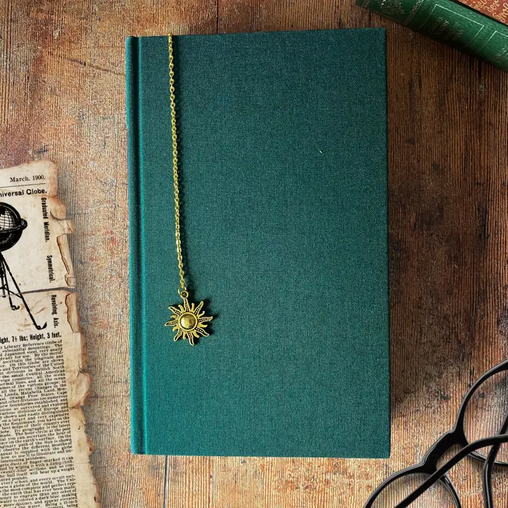 Green notebook with a gold chain bookmark featuring a sun pendant on a wooden surface.