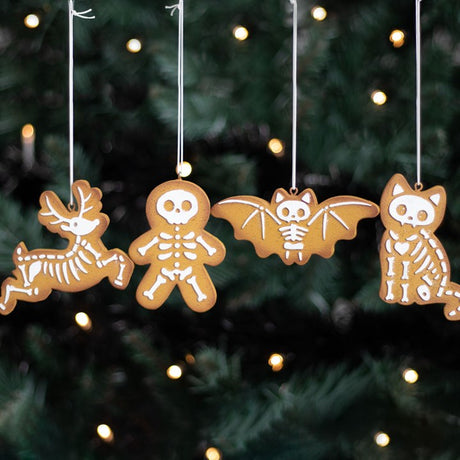 A set of decorative cookie tree ornaments in the shapes of a skeleton, a reindeer, a bat, and a cat, hanging from a Christmas tree with festive lights.
