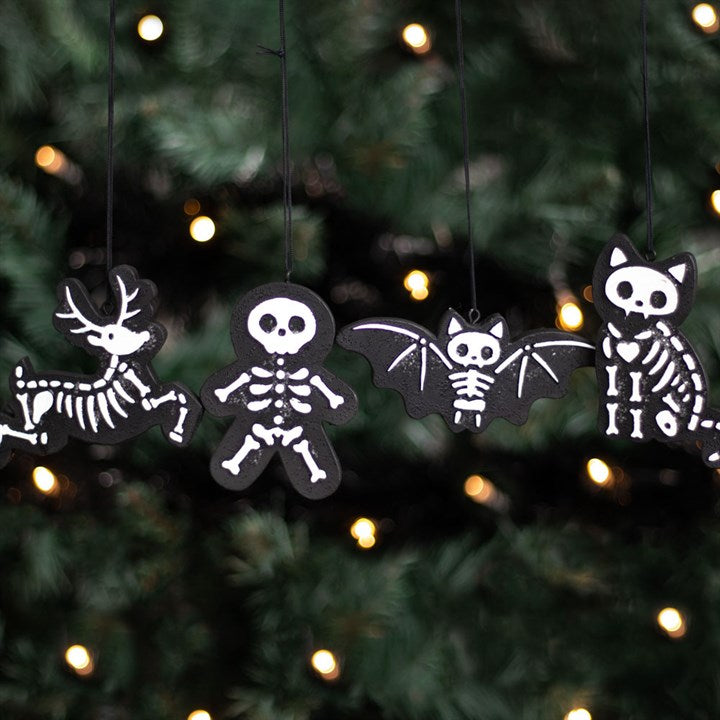 A set of black decorative cookie tree ornaments in the shapes of a skeleton, a reindeer, a bat, and a cat, hanging from a Christmas tree with festive lights.
