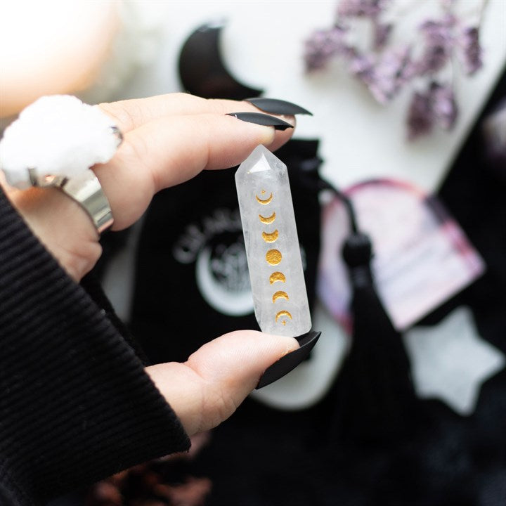 A hand holds a clear quartz crystal point with a gold-tone moon phase engraving