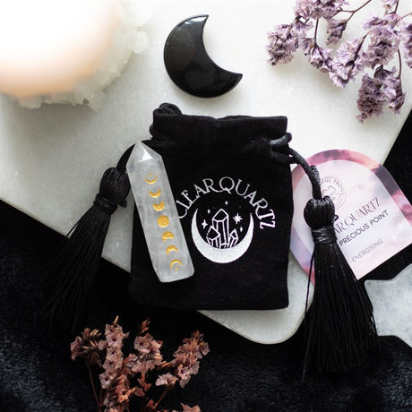 A clear quartz crystal point with a gold-tone moon phase engraving, accompanied by a black drawstring bag