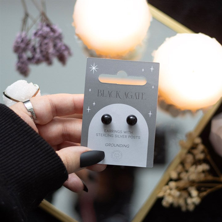 A hand holding black agate crystal stud earrings displayed on a card. 