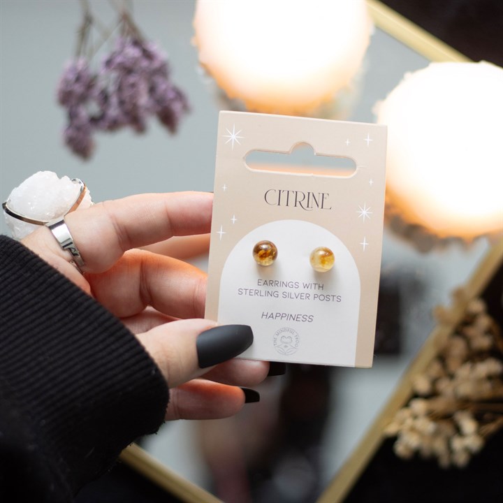 A hand holding Citrine crystal stud earrings displayed on a card. 