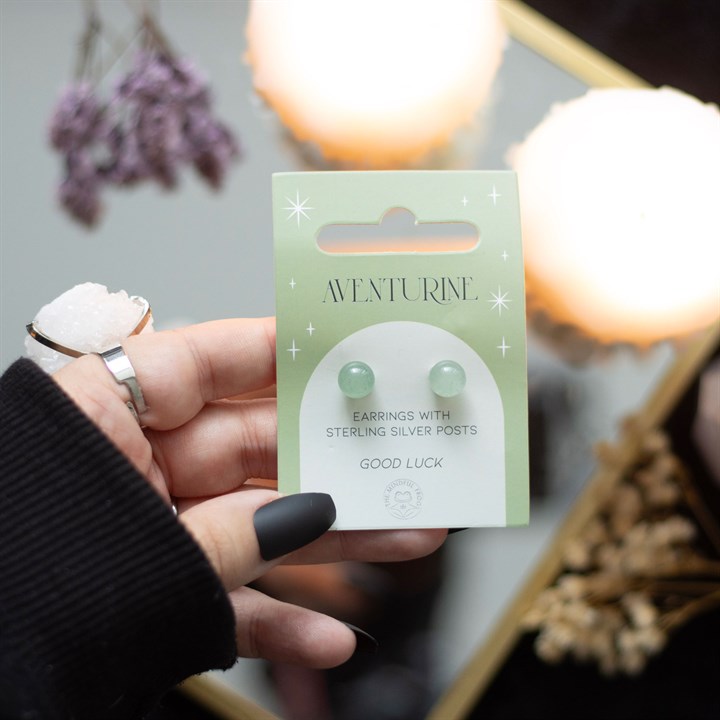 A hand holding aventurine crystal stud earrings displayed on a card. 