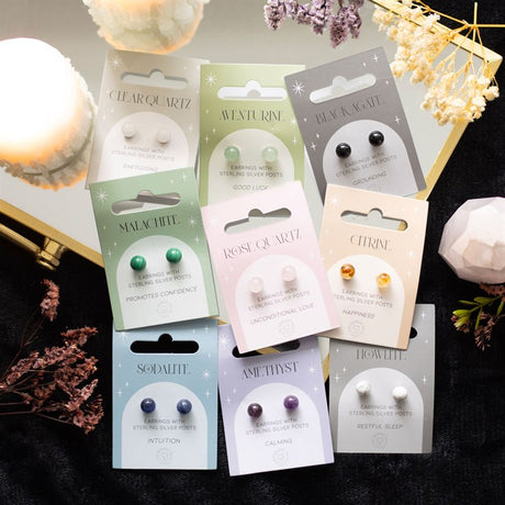 A collection of crystal stud earrings displayed on individual packaging cards, with a variety of colours including purple, black, yellow, clear, green, and pink.