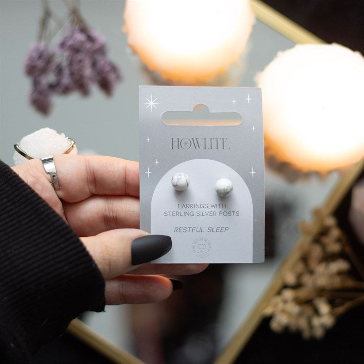 A hand holding howlite crystal stud earrings displayed on a card. 