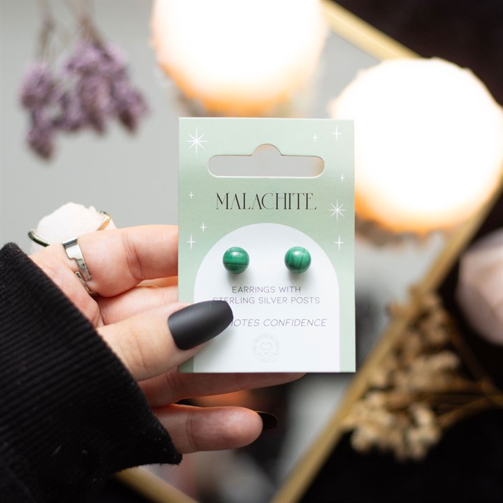A hand holding Malachite crystal stud earrings displayed on a card. 