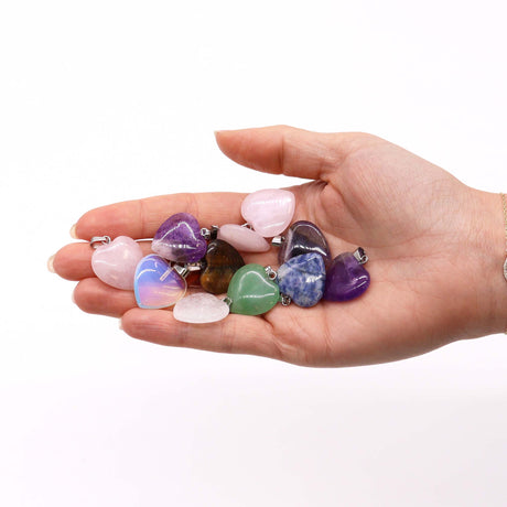 A hand holding several colourful crystal heart pendants 