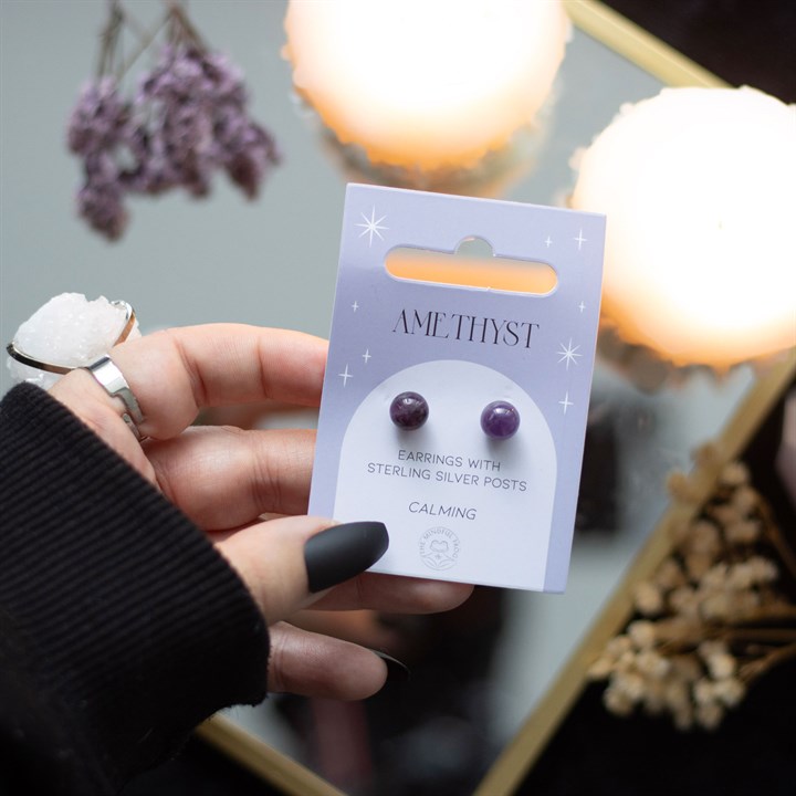 A hand holding Amethyst crystal stud earrings displayed on a card. 
