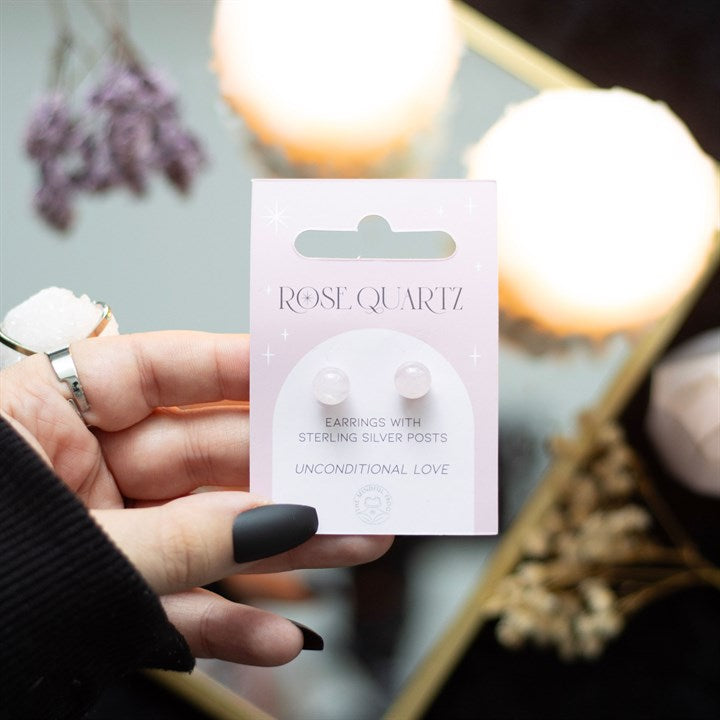 A hand holding rose quartz crystal stud earrings displayed on a card. 