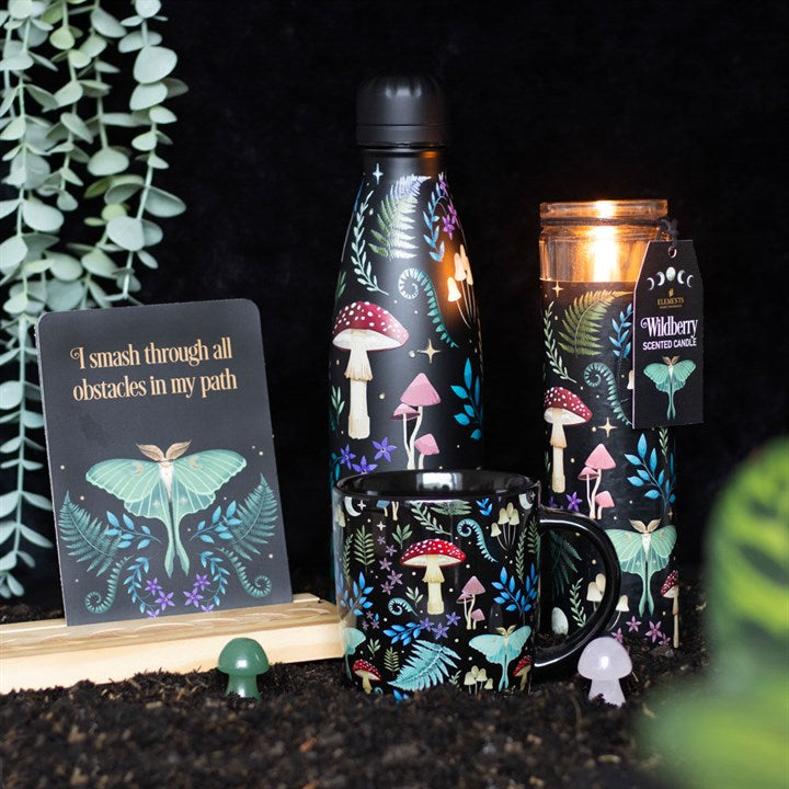 A tube candle with a label 'Wildberry Scented Candle' and an illustration of mushrooms and leaves. The candle is next to other things of the same design such as a water bottle and mug.