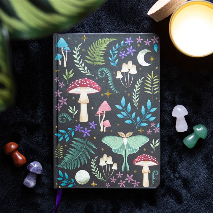 A dark forest mushroom, lunar moth and plant themed A5 notebook on a dark surface surrounded by crystal mushrooms. 