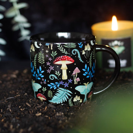 A dark forest, black ceramic mug with a colourful forest and mushroom design, displayed against a candle-lit backdrop.