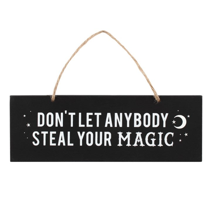 A black hanging wall sign with white text that reads 'DON'T LET ANYBODY STEAL YOUR MAGIC', accompanied by a crescent moon symbol. The sign is displayed against a white background. 