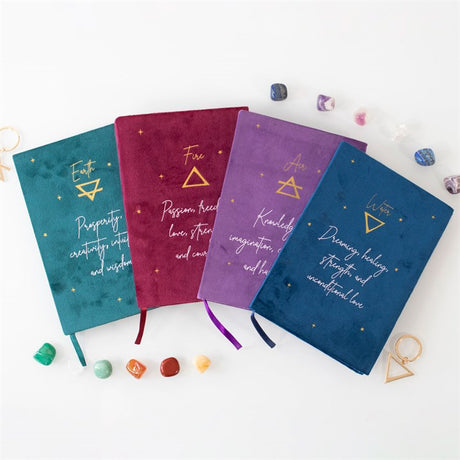 Four A5 notebooks in red, green, purple, and blue velvet covers, each with a different text and starry sky design on the reverse side, representing the elements earth, air, fire, and water.