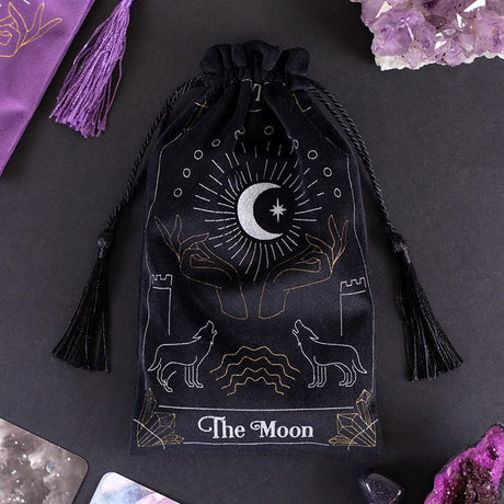 A black silky looking bag with tassels; it has "The Moon" in white font and is decorated with pictures of wolves, castles, hands and the moon