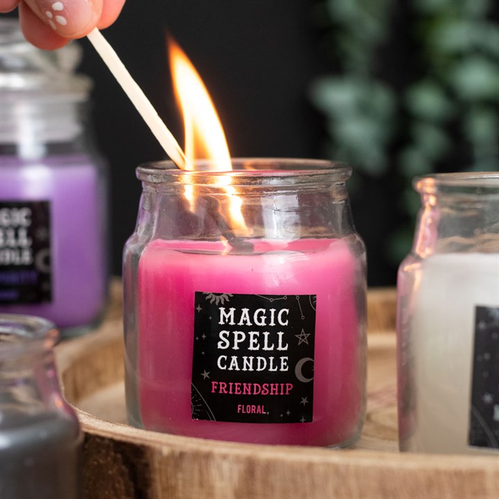 A small lit pink Magic Spell Candles with a label that states it is for "Friendship" and is Floral