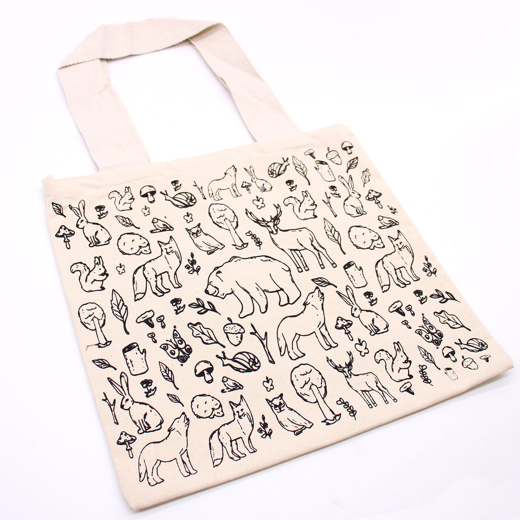 A cream bag which has black lined drawings of various animals such as bears, wolves, hedgehogs, owls, squirrels and some plant life such as acorns, trees and herbs