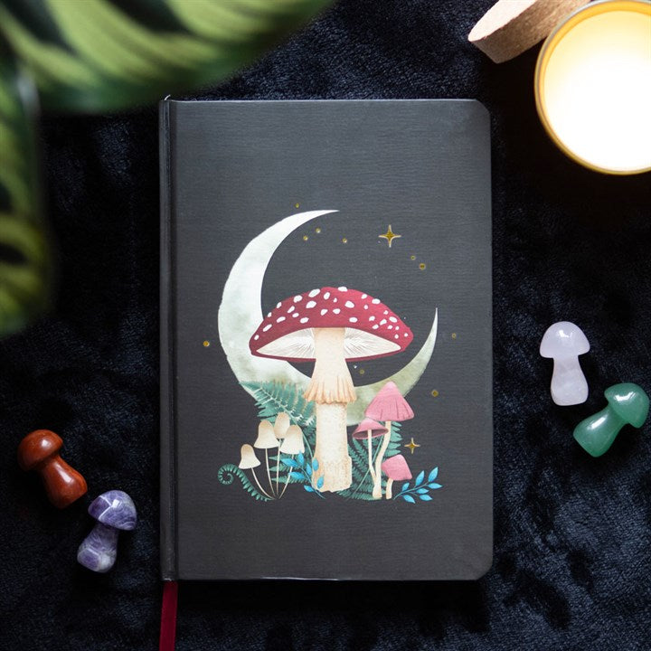 A mushroom and crescent moon themed A5 black notebook on a dark surface surrounded by crystal mushrooms. 