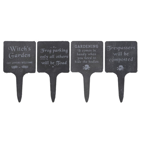 A set of four dark slate garden signs with humorous phrases related to witchcraft and gardening, each with a metal stake for inserting into the ground.