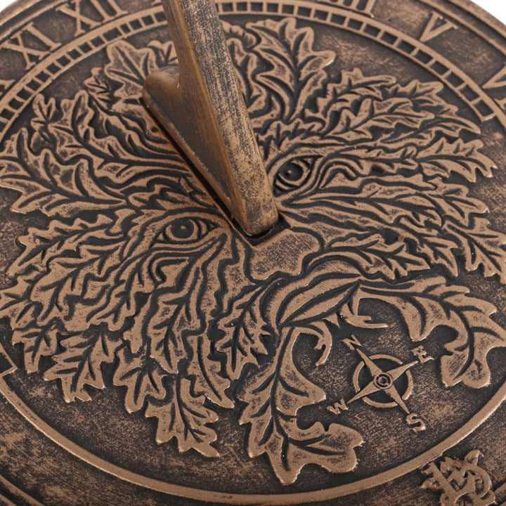 A close up of green man themed sun dial laid on a white surface 