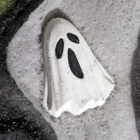 Ghost-shaped bath bomb with black eyes on a sandy surface