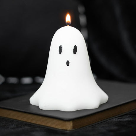 A ghost-shaped candle on a book, with a lit candle showing through the ghost shape, creating a spooky Halloween decoration.