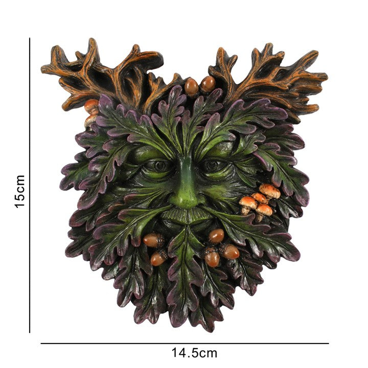 A small face-shaped plaque featuring a green man design with leaf patterns, acorns, and toadstools against a white background with measurement indicators 