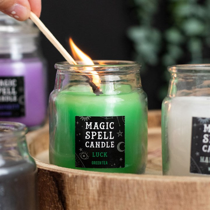 A small lit green Magic Spell Candles with a label that states it is for "Luck" and is Green Tea