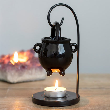 A black hanging cauldron-shaped oil burner with a lit candle below, placed on a flat surface.