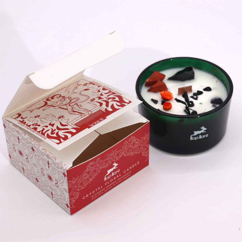 Viewed from the side: a green glass candle with red and orange dried flowers and red and black crystals. There is also a matching "devil" box.