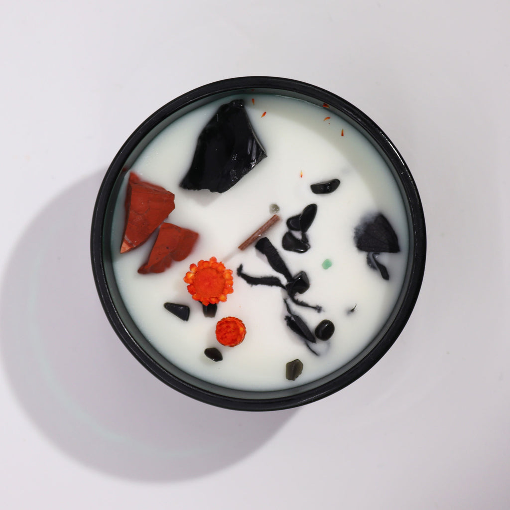 Viewed from above: a green glass candle with red and orange dried flowers and red and black crystals.