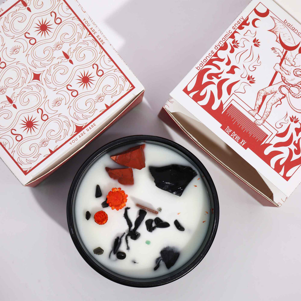 Viewed from above: a green glass candle with red and orange dried flowers and red and black crystals. There are also matching "devil" boxes.