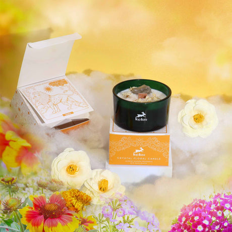A crystal magic flower candle named 'The Lion' by Hop Hare, displayed with an open box showing a tarot card, set against a floral background. The candle is adorned with dry flowers and Rock Quartz.