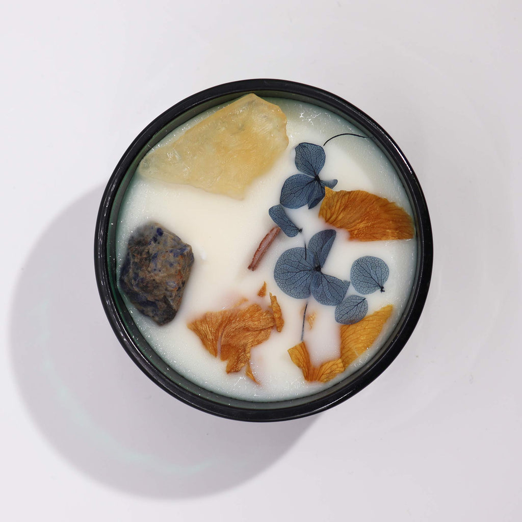 Viewed from above: a green glass candle with natural flowers, blue and yellow gemstones embedded in it.