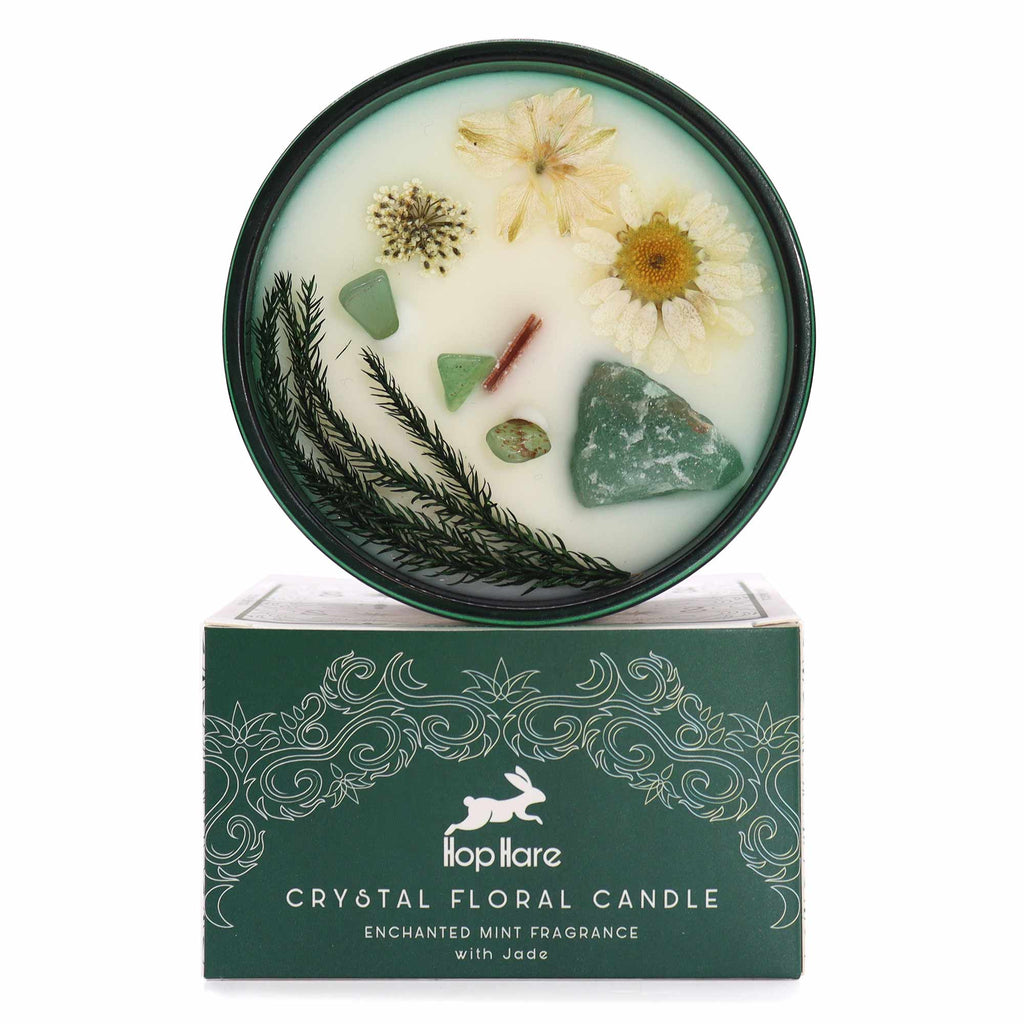 Viewed from above: A green glass crystal magic flower candle, adorned with dry flowers and jade gemstones. It is above its matching green and white box. 