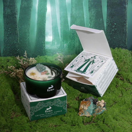 A green glass crystal magic flower candle named 'The Magician' by Hop Hare, displayed next to its packaging box on a mossy surface. The candle is adorned with dry flowers and jade gemstones. 