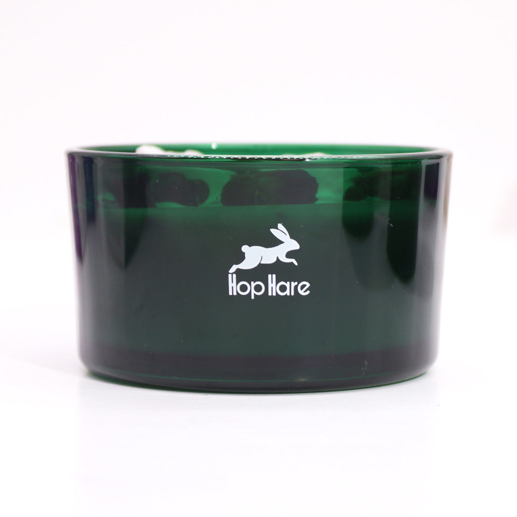 A green glass candle with a white HopHare design. 