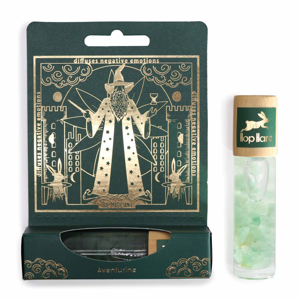 A product image featuring a roll-on essential oil bottle with gemstone chips inside, alongside a green box with gold-printed tarot card.