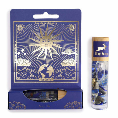 A product image featuring a Hop Hare essential oil gemstone roll on named 'The Sun'. It includes a roll-on bottle with blue and white gemstones visible through the clear part of the bottle, and a tarot card with gold printing displayed above it, set against a blue packaging with sun and clouds design.