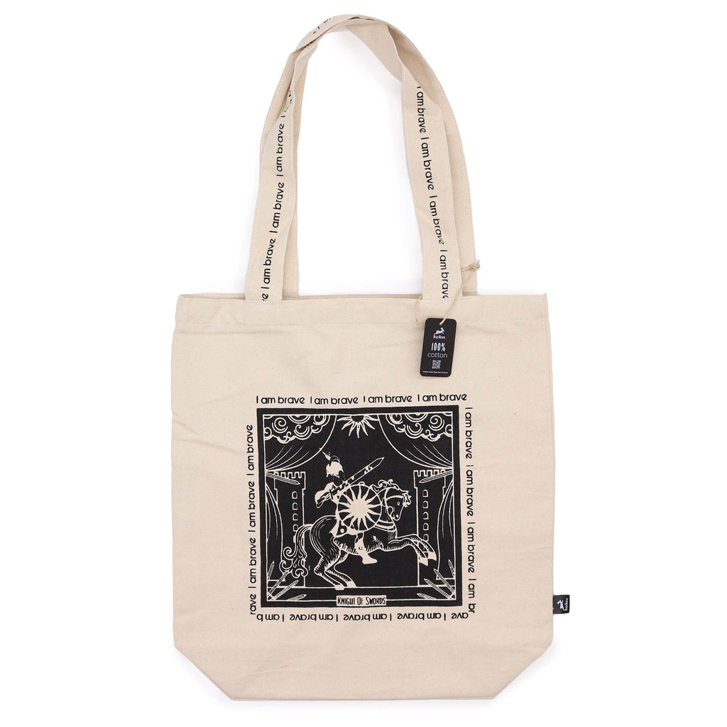 Tote bag with black motif which is of a "knight on a horse" standing in front of a castle with the affirmation "I am brave" repeated around the motif. 