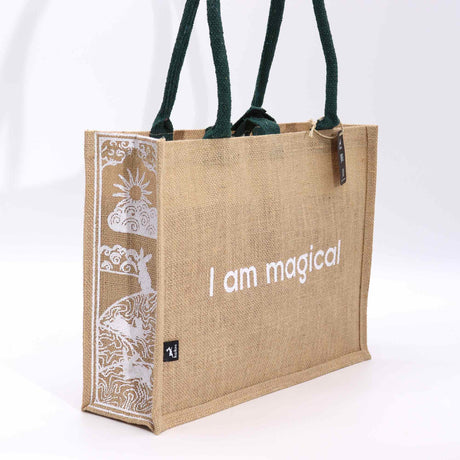 A beige jute bag, with green handles, with the text 'I am magical' printed on the side, featuring a moon and hare design.